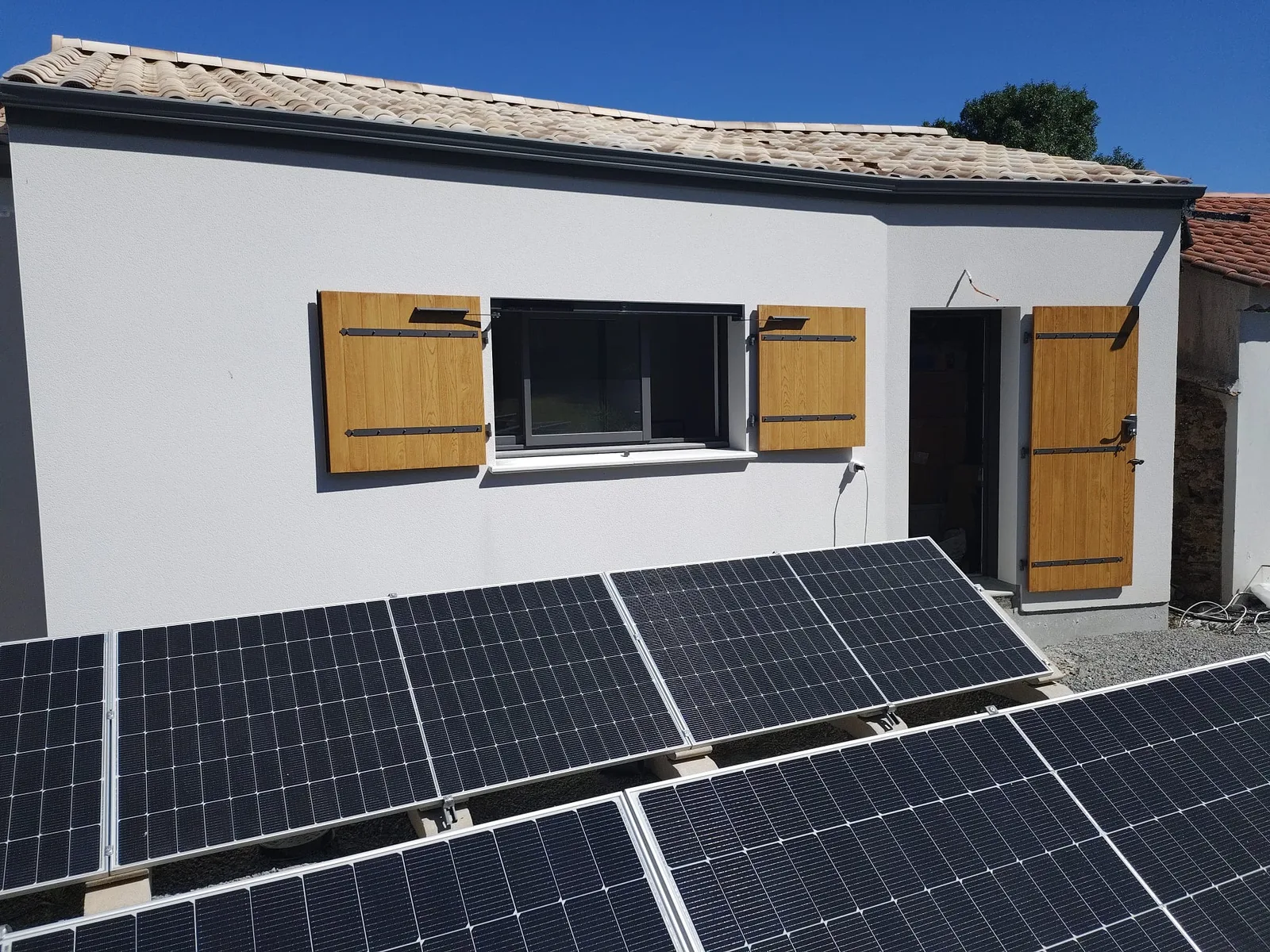 Volets battants aspect chêne clair sur une façade équipée de panneaux solaires
