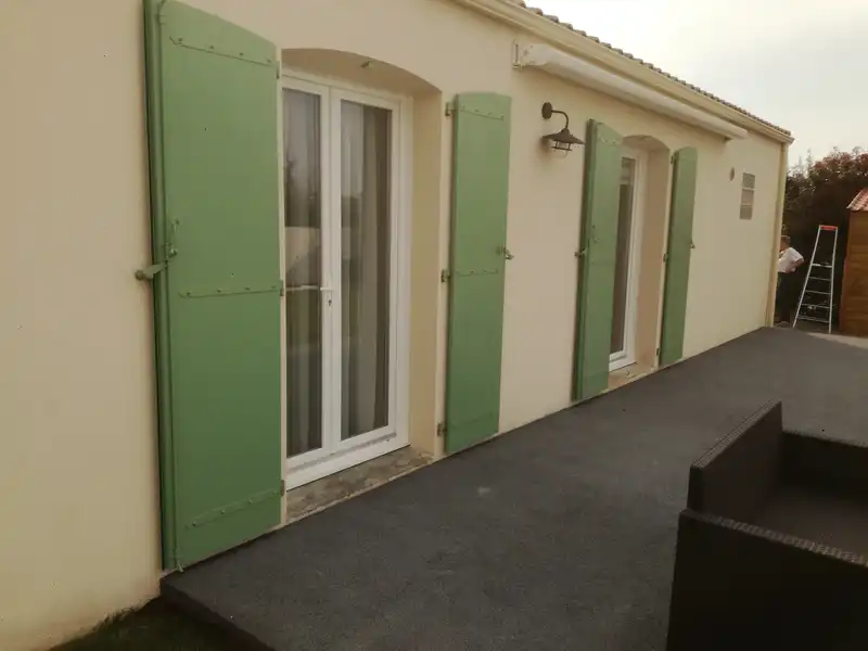 Ouvertures arrondies et volets battants verts sur mesure sur une façade claire
