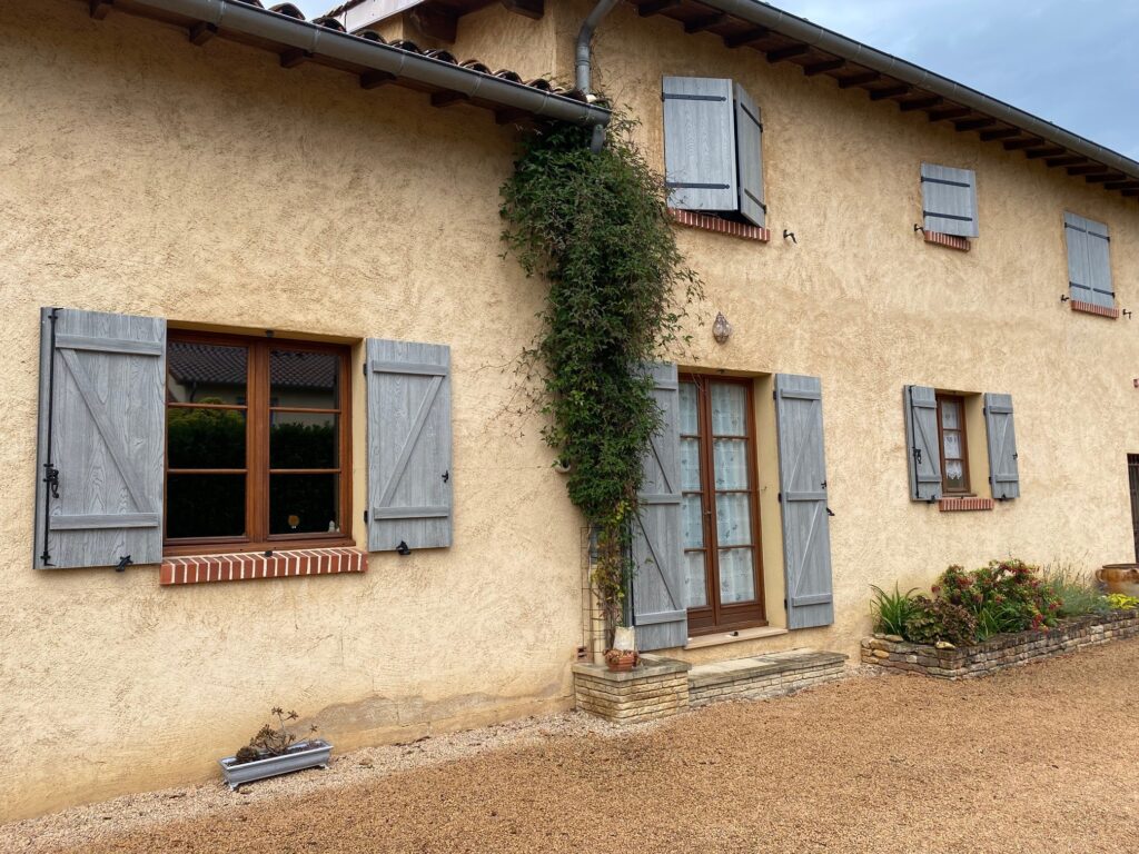 Volet battant isolant gris autour des fenêtres d’une maison en enduit beige