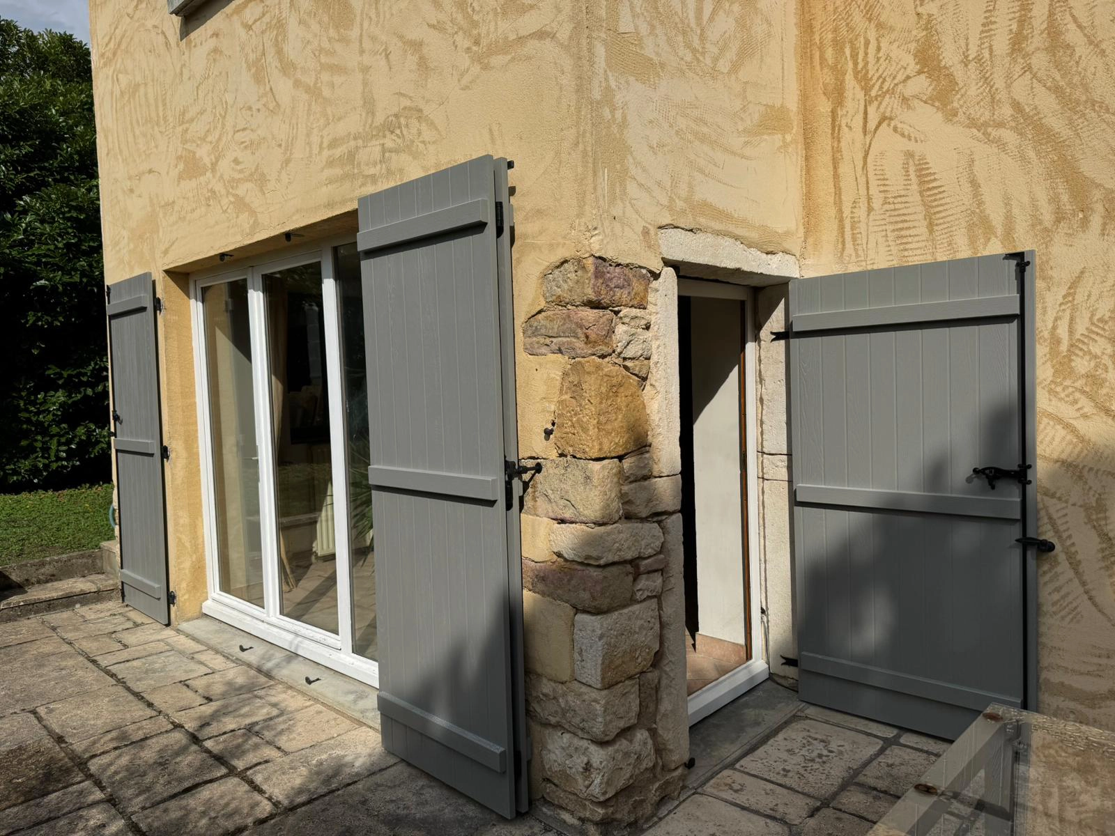 Volets pleins gris ouverts sur une façade ocre