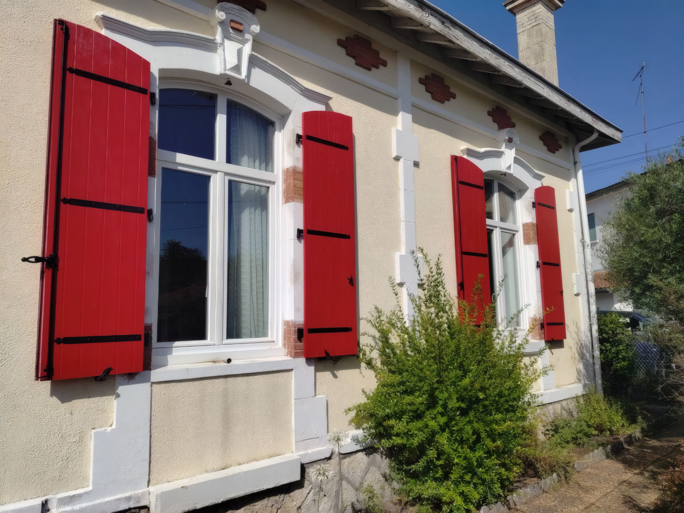 Façade claire avec plusieurs volets battants rouges